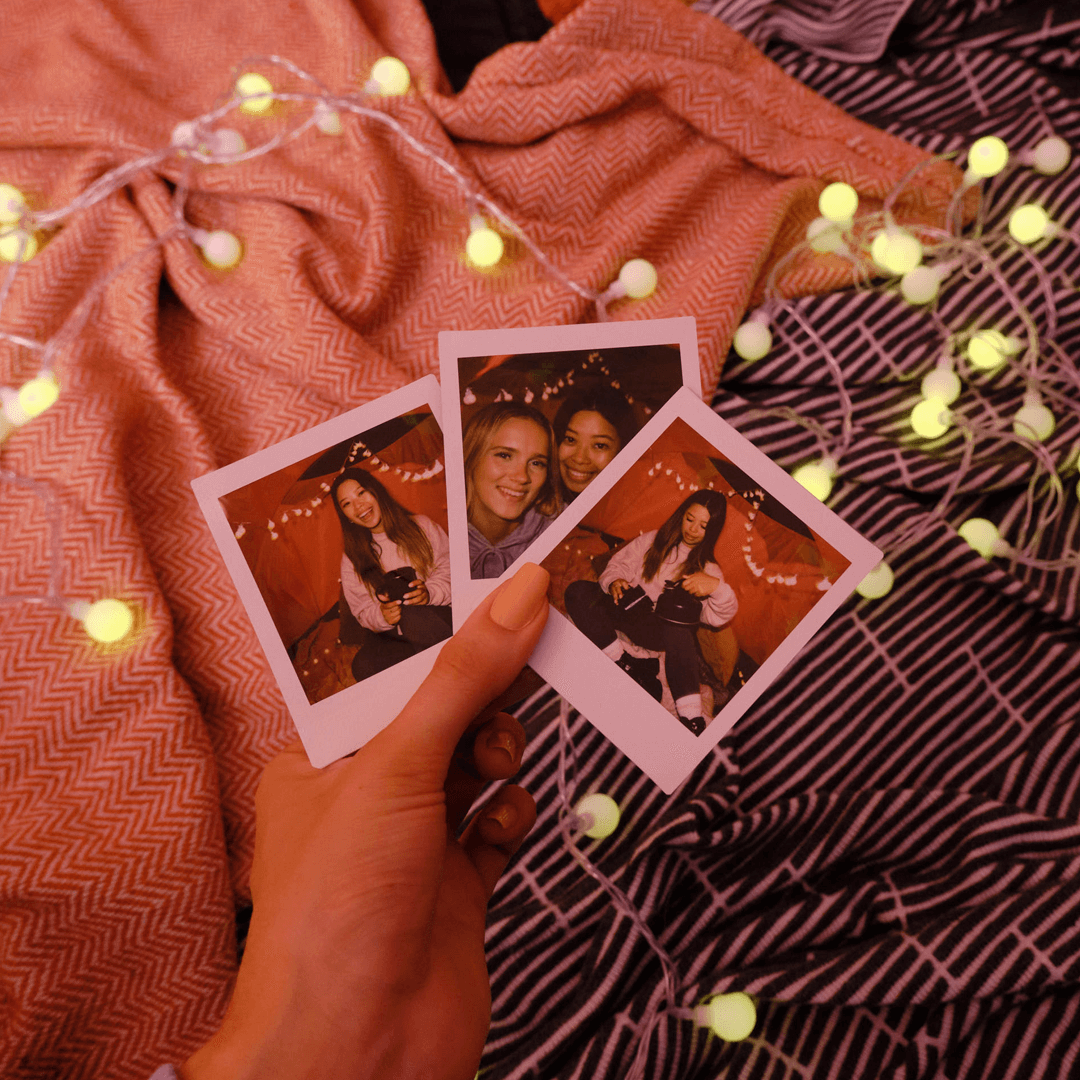 Sfeerafbeelding instax™ SQUARE film met lichtjes op dekens en 3 foto's met meiden die een gezellige avond hebben