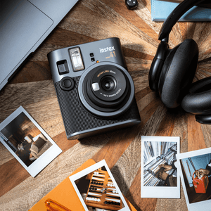 Instax mini 41 camera vooraanzicht op een tafel met fotos, een koptelefoon en de onderkant van een macbook in beeld