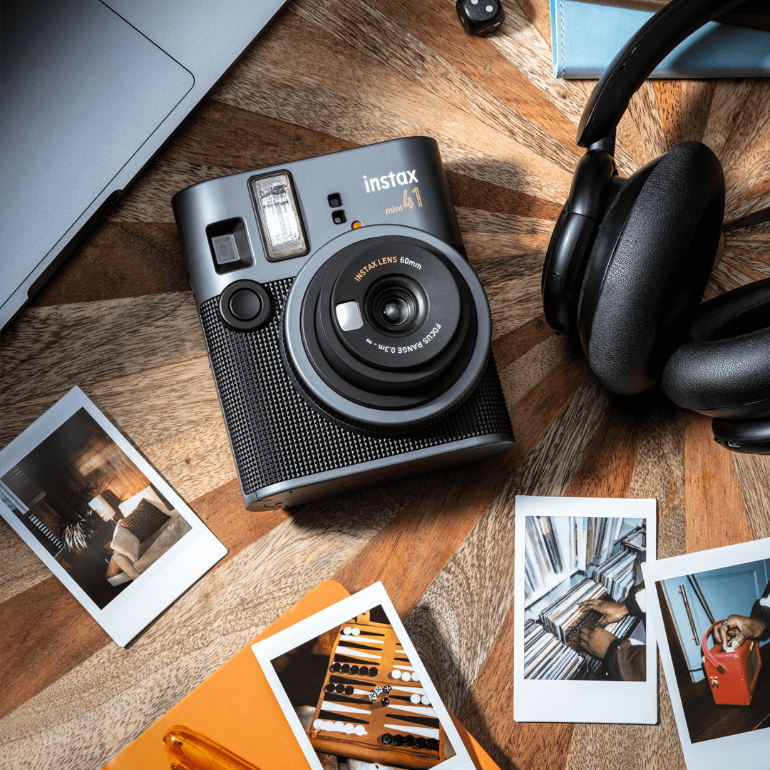 Instax mini 41 camera vooraanzicht op een tafel met fotos, een koptelefoon en de onderkant van een macbook in beeld