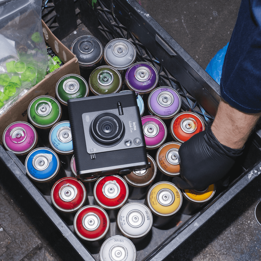 Instax WIDE EVO™, op een krat met spuitbussen in diverse kleuren