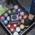 Instax WIDE EVO™, op een krat met spuitbussen in diverse kleuren