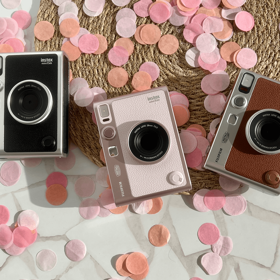 instax mini Evo in zwart, roze en bruin op de foto. Op de achtergrond ligt confetti op een marmeren tegel.